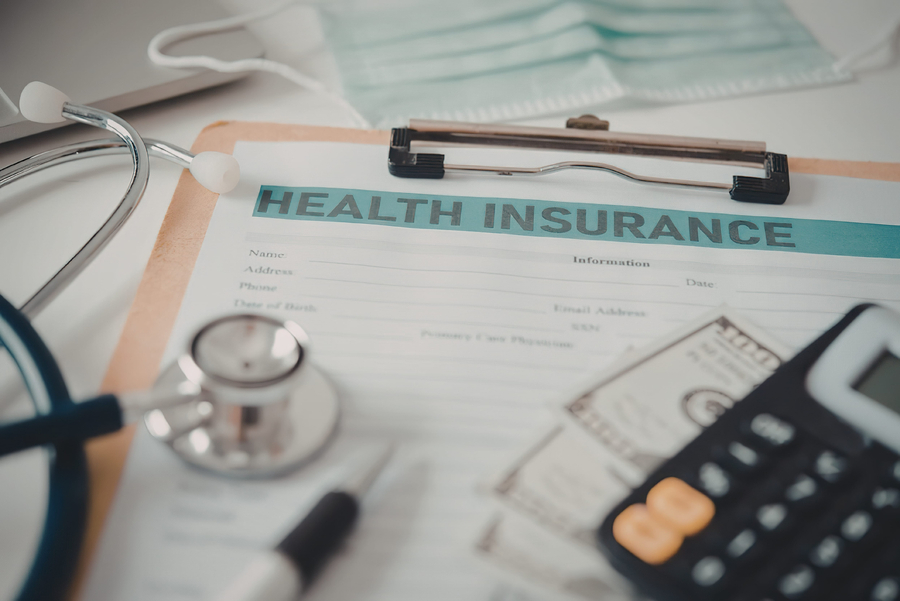 A clipboard with health insurance documents, stethoscope, calculator